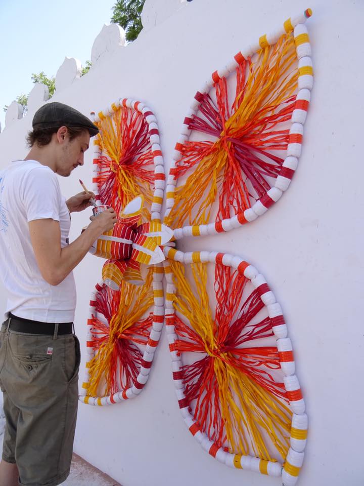 Kunststudent Alex arbeitet an seinem Kunstwerk, das an einer Wand im öffentlichen Raum Palis aufgehängt wurde. Es ist vollständig aus alten Plastikflaschen hergestellt.jpg